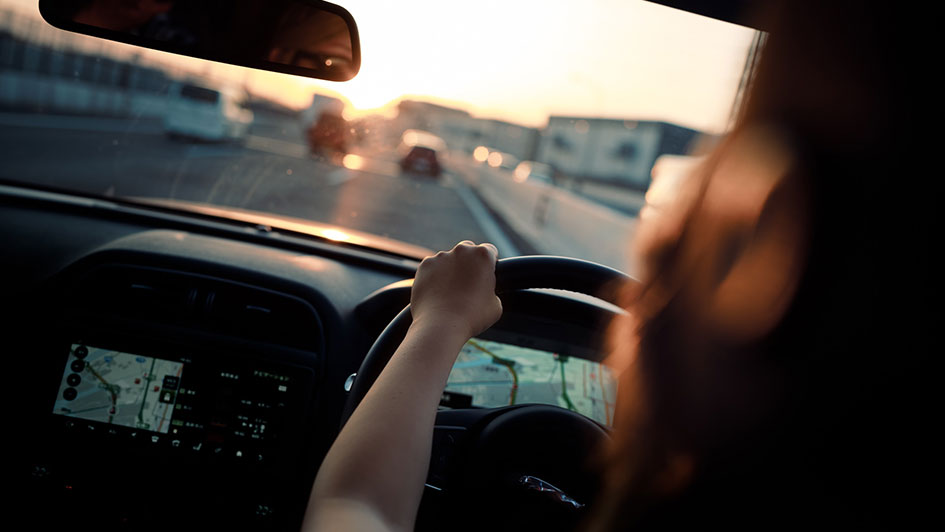 Eine junge Frau fährt mit ihrem Auto der Sonne entgegen